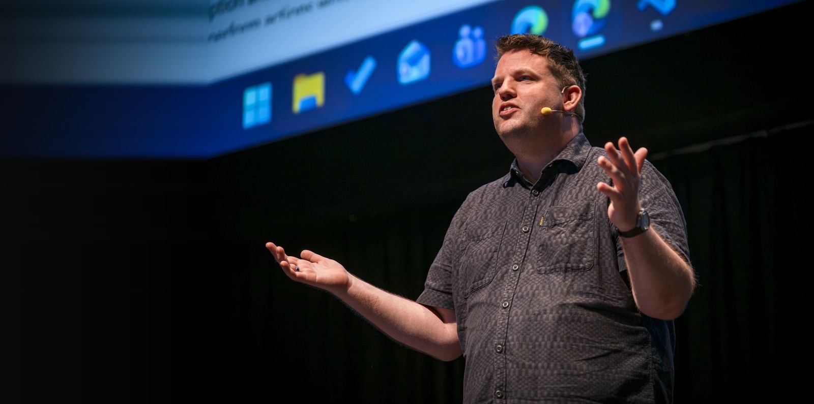 Daniel Laskewitz mid-sentence on stage at the European Power Platform Conference 2026, hands open, a slide of Microsoft 365 icons behind him.